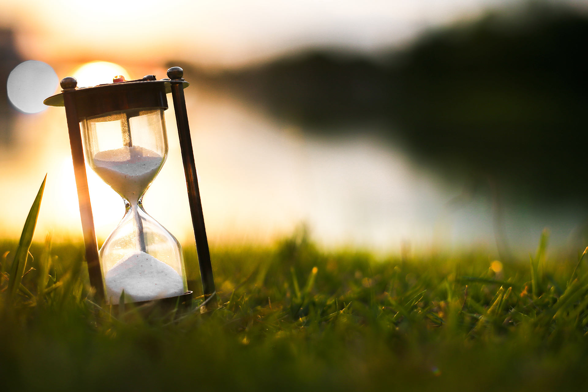 Eine Sanduhr auf einer Wiese vor einer untergehenden Sonne